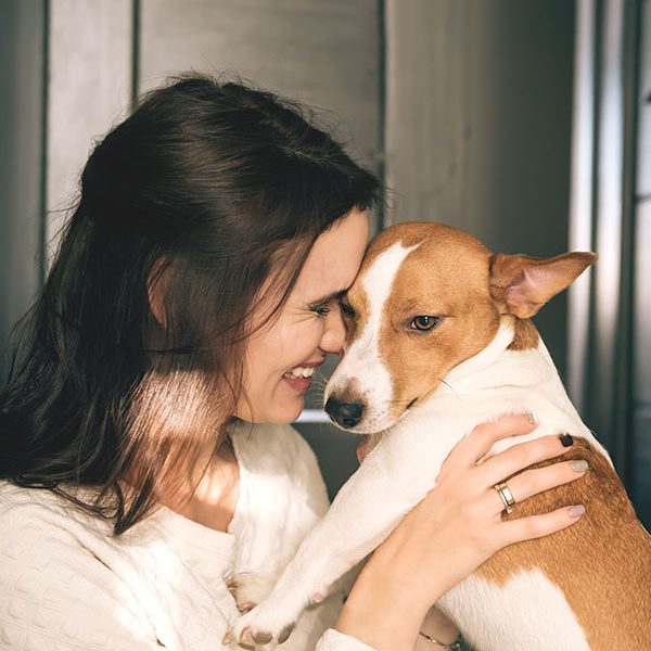 Young beautiful smiling woman hugging her dog at home